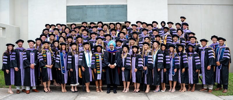 76 graduates stand with the dean on some steps.