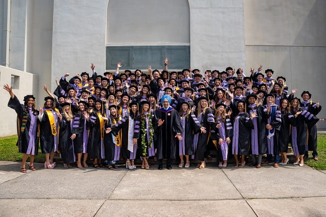 The 78 graduates, dressed in the purple-striped regalia of dentistry, throw their hands in the air in celebration, joined by the dean.