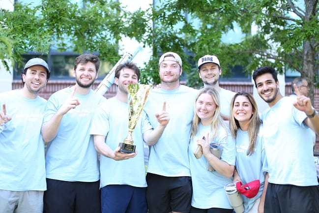 Eight dental students wearing matching "Field Day" tshirts hold up a golden trophy or hold up a finger to show they came in first place.