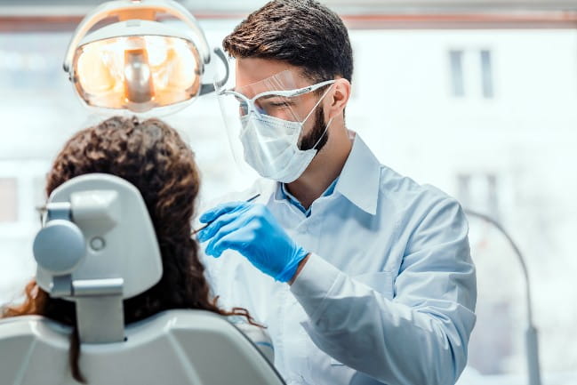 Masked care team member examining the mouth of a dental patient